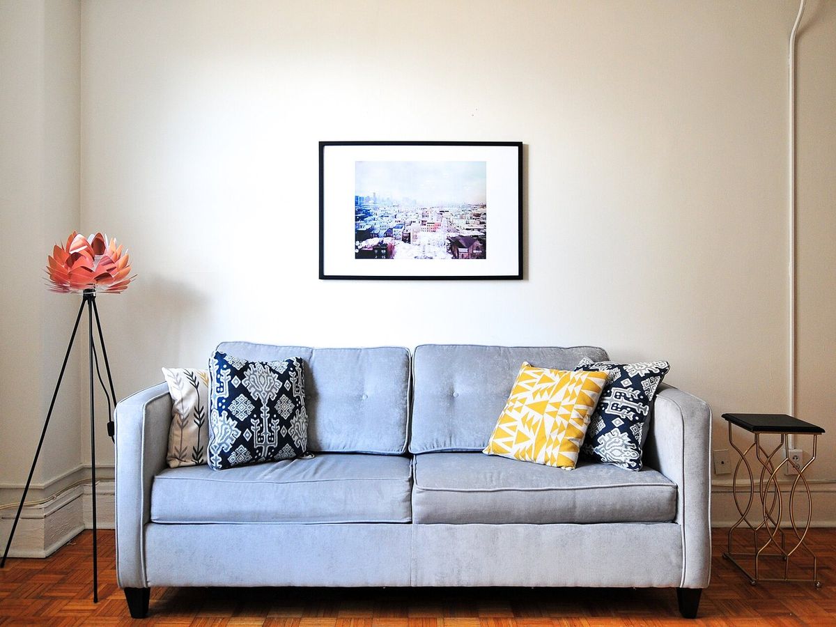 A living room with a light blue sofa, wood floors and a framed picture on a cream wall