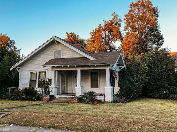 A one-story wood bungalow with a front porch and autumn trees in Old East Dallas