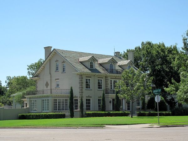 A large cream-colored house with dormer windows and a wide green lawn on Swiss Avenue